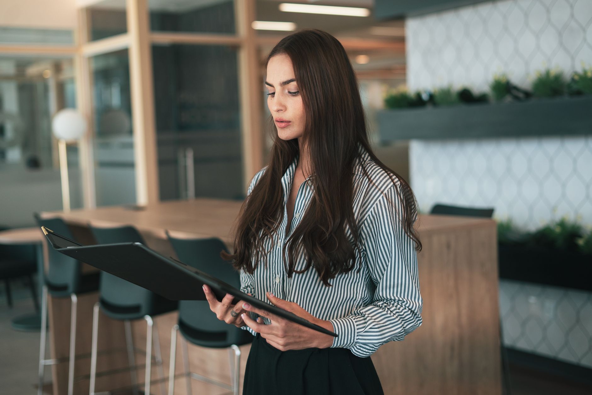 Focused businesswoman reviews documents in a modern office setting, showcasing corporate professionalism.