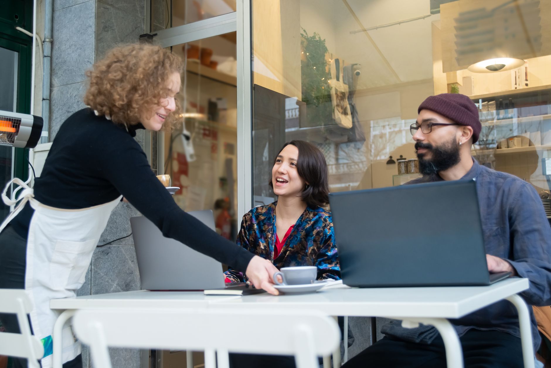Two adults working remotely at a Portugal café, served by a waitress.