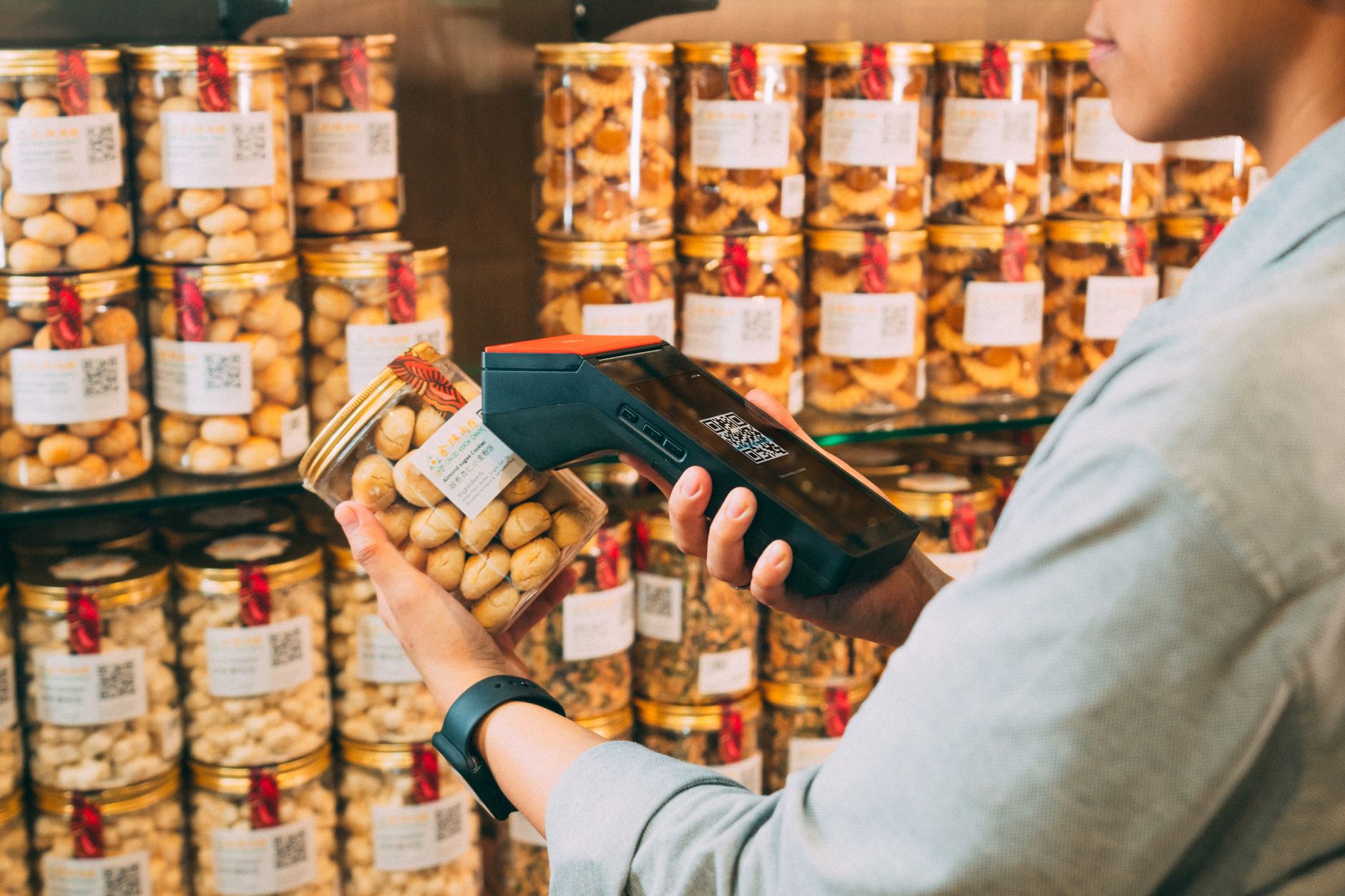 Individual scanning QR codes on jars in a store with a handheld device.